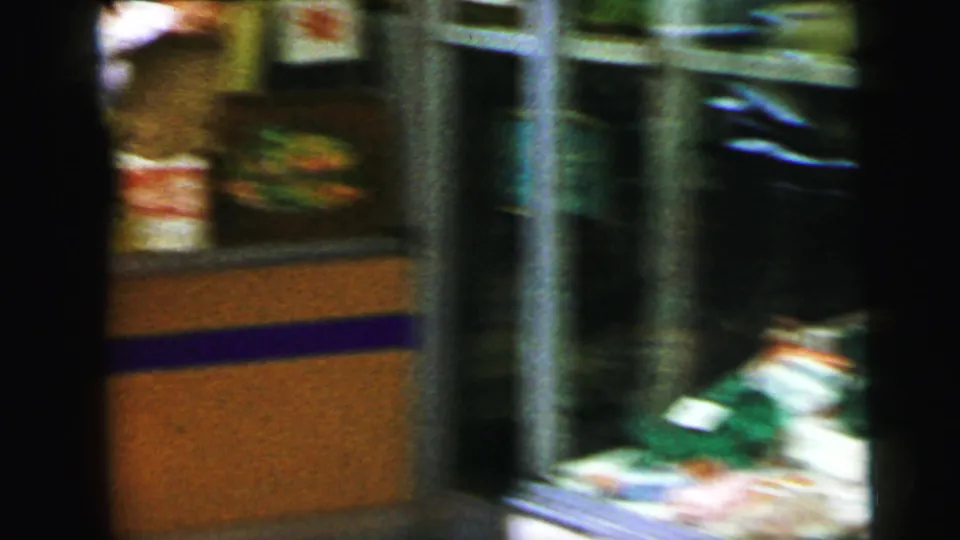 Motion-blurred 8mm frame of a retail display interior, likely Camden, NJ, 1964; colorful products and an orange-brown counter visible.