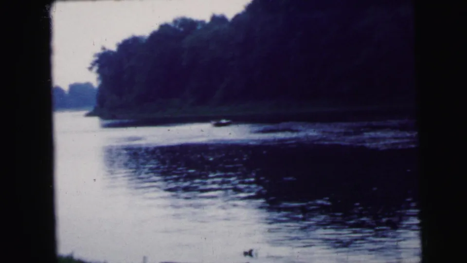 Wide pan of calm river with tree-lined far bank and pale overcast sky; 8mm home movie attributed to Camden, New Jersey, 1964.