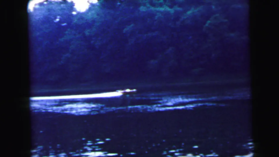 Motorboat leaving a prominent white wake across a wide river, varied tree line on far shore; 8mm home movie attributed to Camden, New Jersey, 1964.