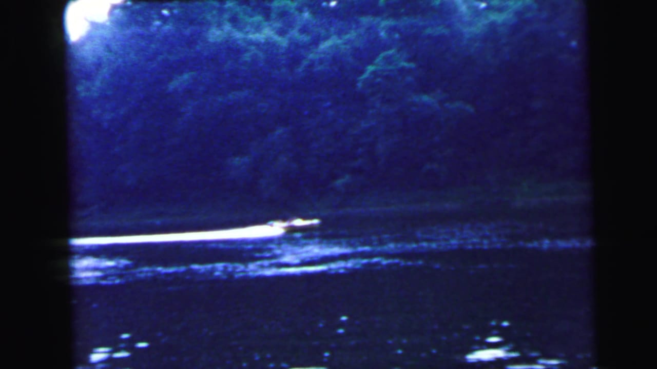 Small motorboat crossing a dark blue lake with a dense forested treeline on the far bank