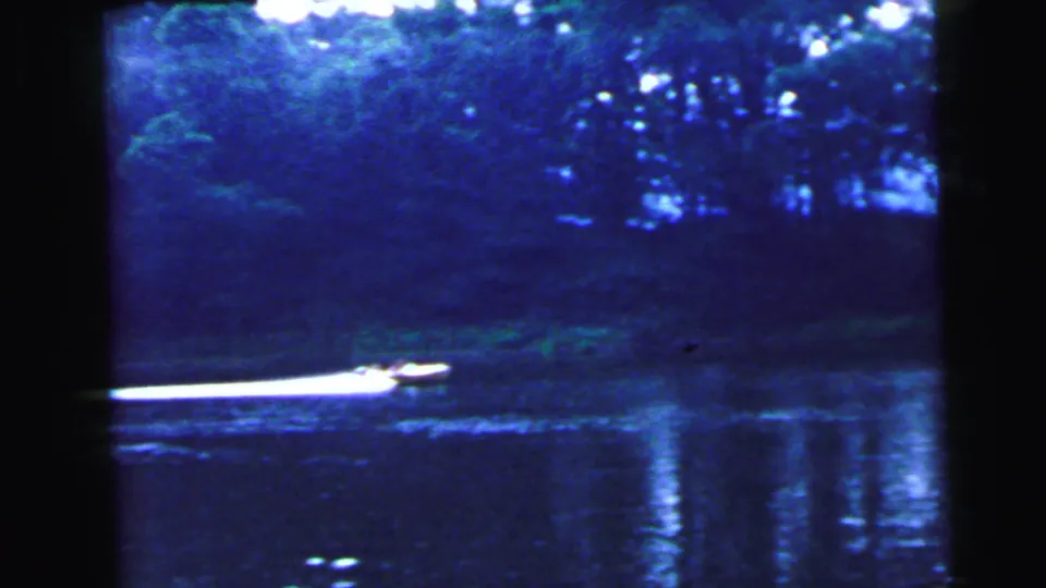8mm home movie c.1964 showing a motorboat mid-crossing on a dark blue lake with reflected treeline, consistent with a New Jersey waterway