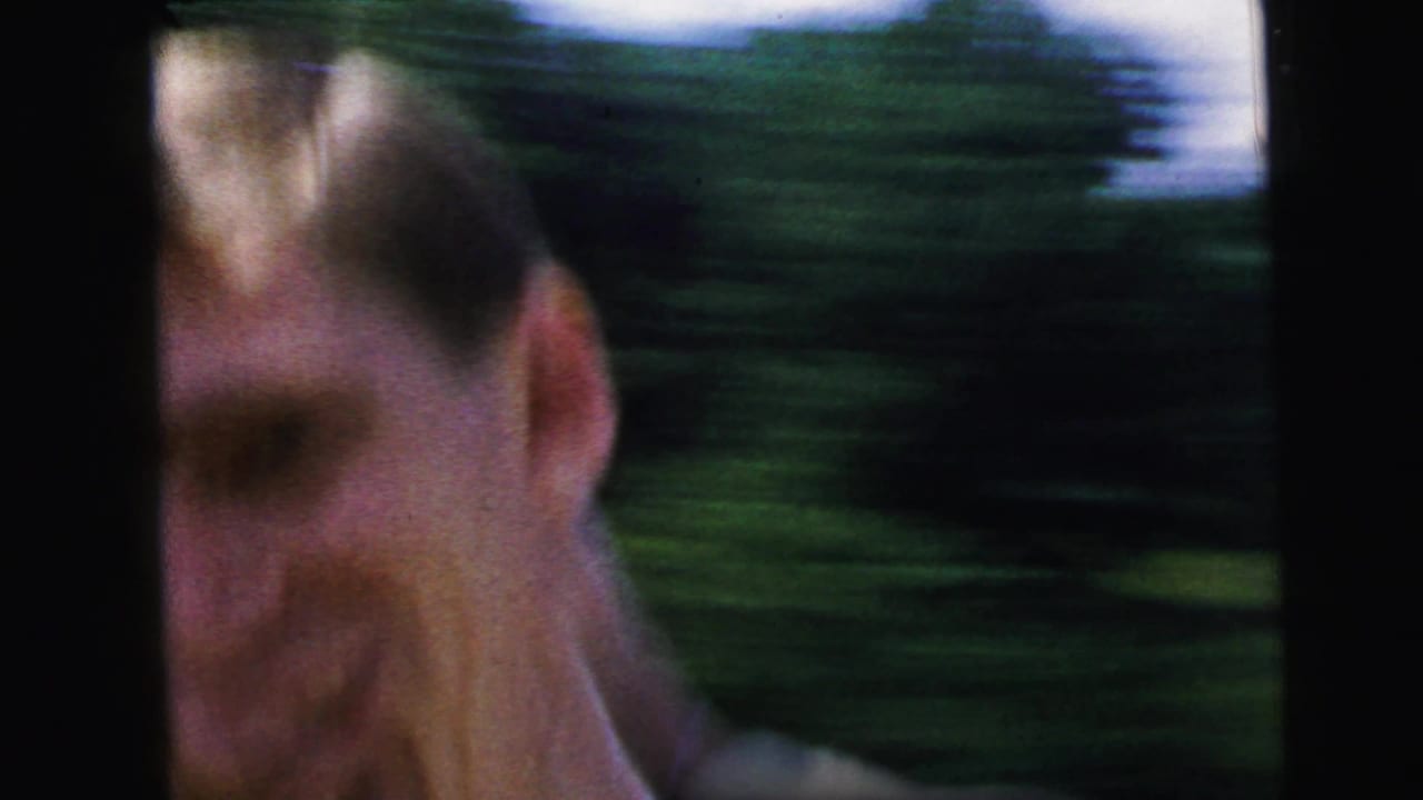 Blurred close face in handheld 1964 Camden home-movie footage, with green outdoor background streaked by camera movement.