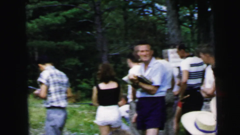 Casually dressed people gather outdoors near trees in 1964 Camden home-movie footage, with faces partially visible.