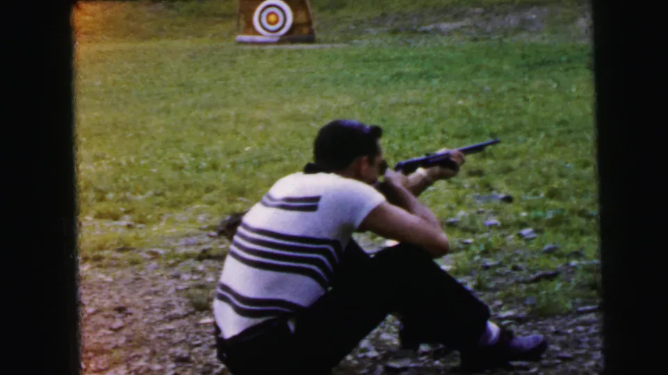 Adult man in horizontal-striped shirt continues aiming rifle at an outdoor range; consistent 8mm framing throughout this brief clip; 1964 home movie, Camden, New Jersey.