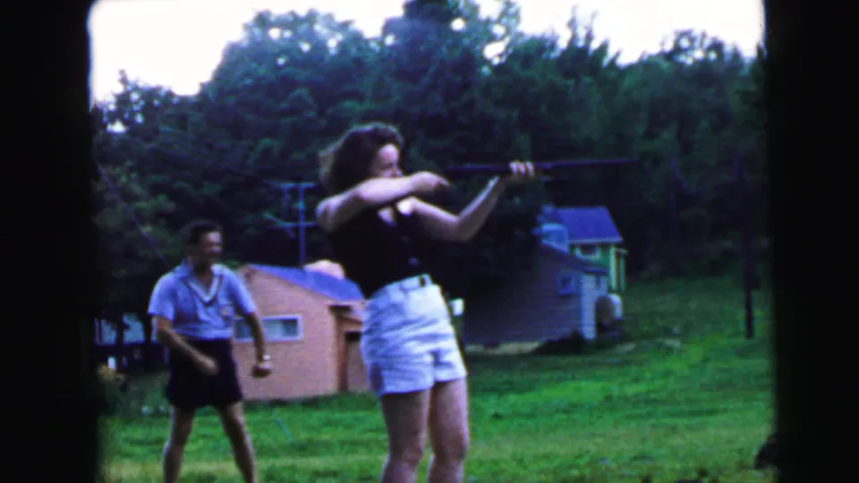 8mm home movie still, c.1964, possibly Camden NJ: young woman in firing or follow-through position with rifle, male companion moving forward.