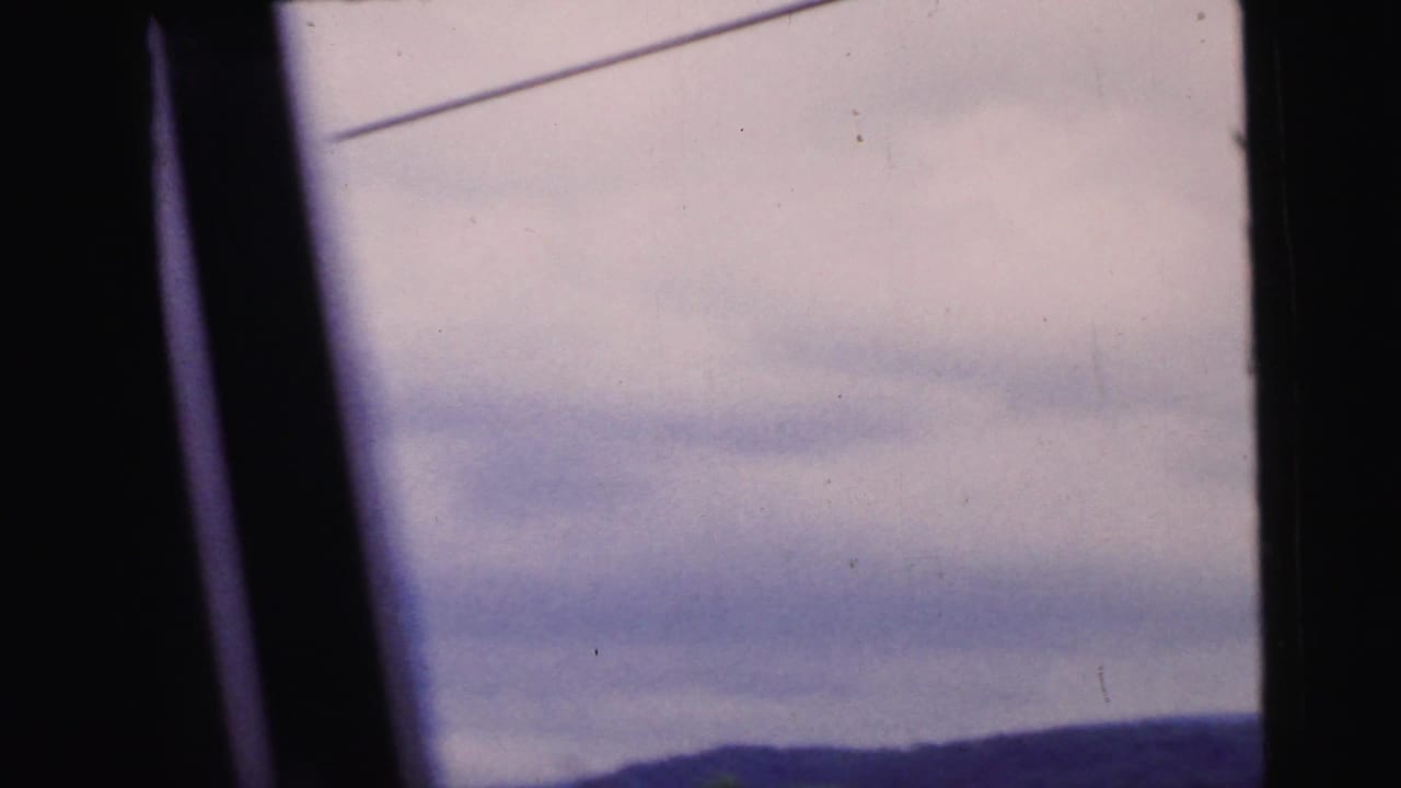 View through a car window of an overcast sky and distant wooded hillside, with a utility wire crossing the upper frame diagonally.