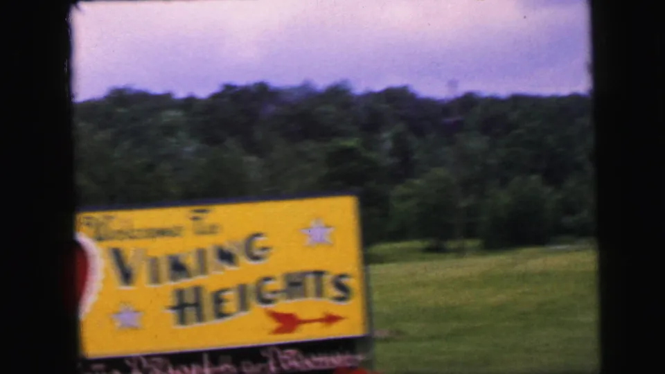 8mm home movie frame circa 1964 showing the Viking Heights sign in close-up from a moving vehicle, with bold text, red arrow, and star motifs clearly legible despite gentle motion blur.