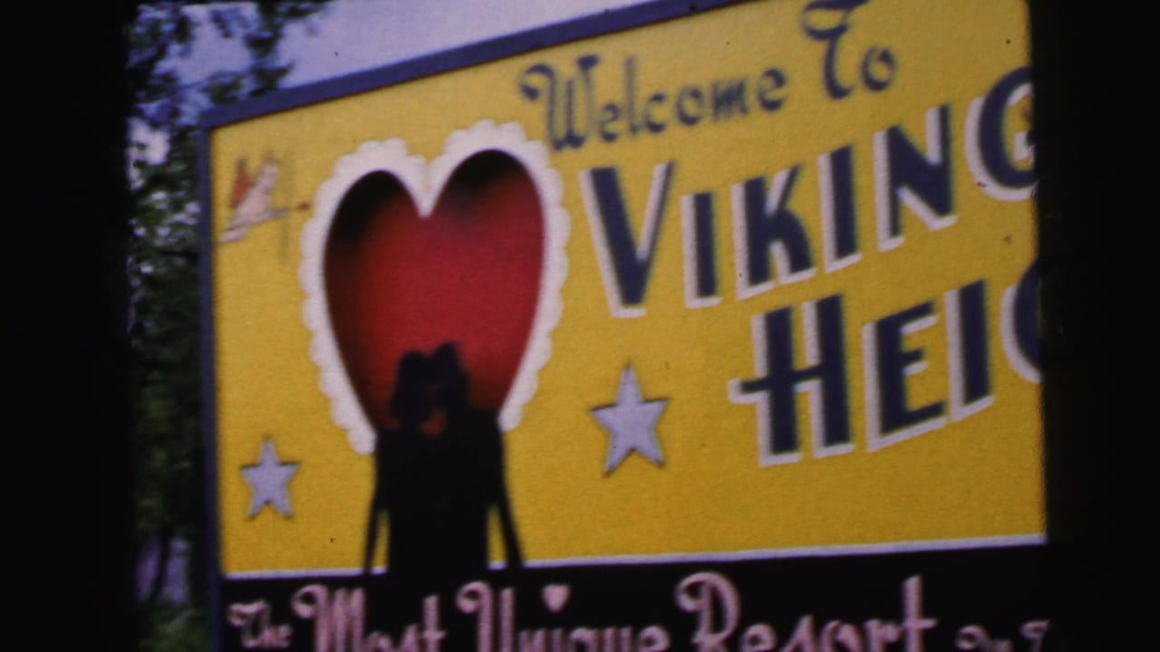 Close-up of the Viking Heights entrance sign circa 1964: yellow board with 'Welcome To' in cursive, bold 'Viking Heights,' red heart motif with silhouette, two stars, and resort tagline below.