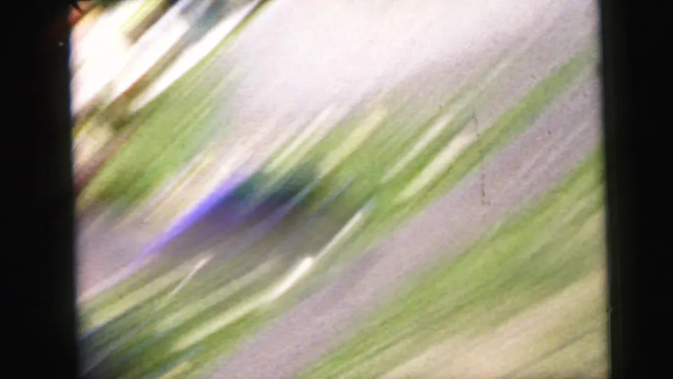 Motion-blurred 8mm transitional frame; diagonal green and white light streaks from rapid camera movement obscure any distinct subject.