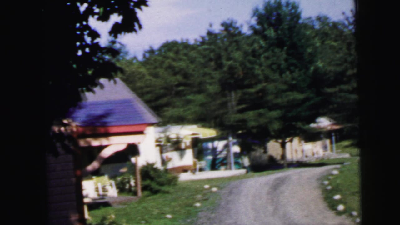 Gravel driveway and open pavilion with purple roof, near-identical to preceding frame as camera advances slowly forward.