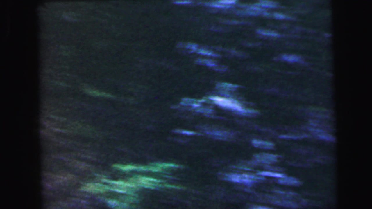 Out-of-focus blue-green vegetation or water reflection, opening frame of a 1964 8mm road clip identified in metadata as Camden, New Jersey.