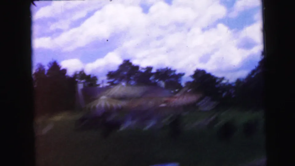 8mm home movie circa 1964: sky view through vehicle window showing cumulus clouds over treetops along a rural road, likely continuing from the resort entrance approach.