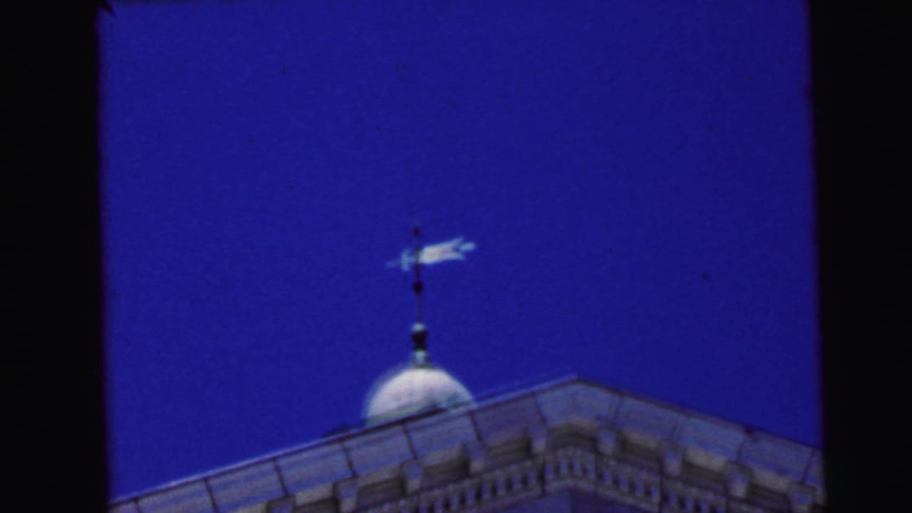 Domed cupola with arrow weather vane against a deep, saturated blue sky, with a triangular roofline below