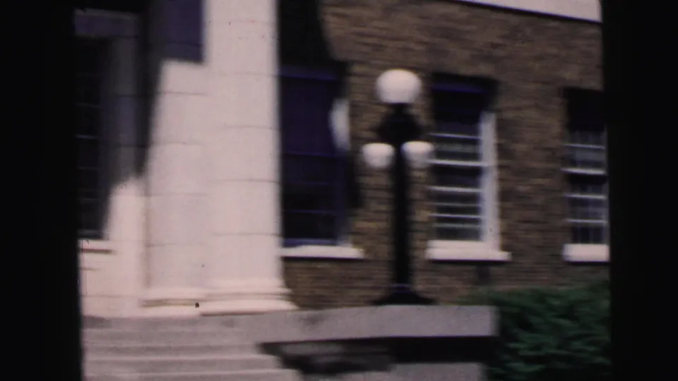 Courthouse exterior grounds with globe lamp cluster, white column, entrance steps, and neighboring brick building, Camden, New Jersey, 1964, 8mm film