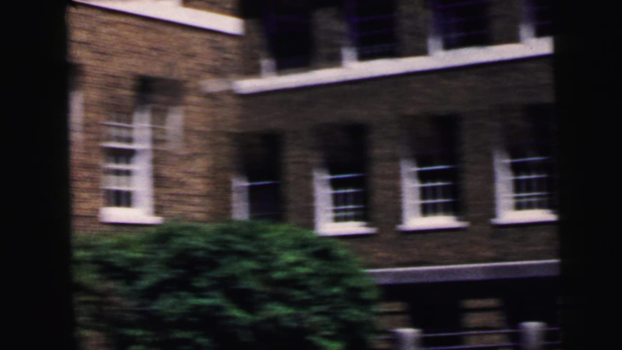 Exterior of a multi-story dark brick building with white-trimmed windows and green tree at left; 8mm home movie, Camden NJ area, circa 1964