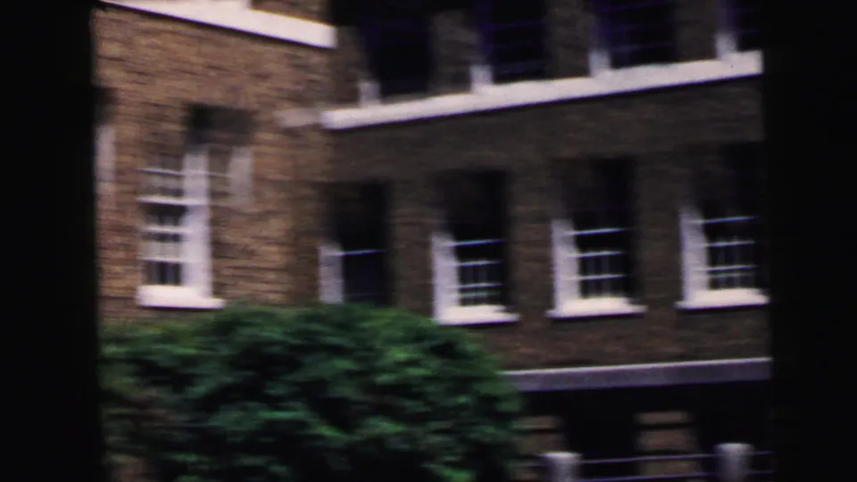 Exterior of a multi-story dark brick building with white-trimmed windows and green tree at left; 8mm home movie, Camden NJ area, circa 1964