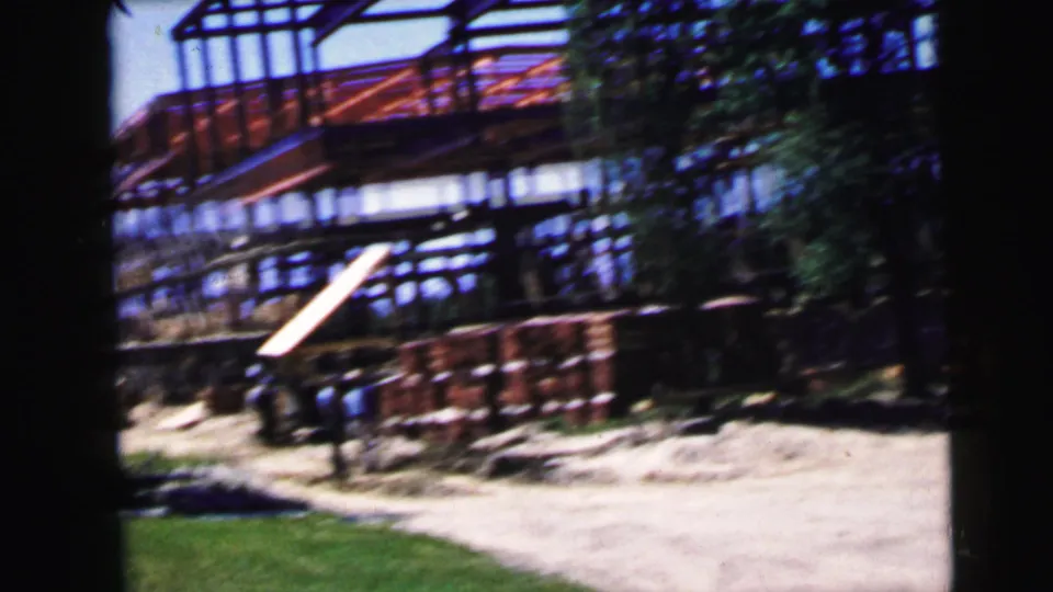 Active construction site with red steel structural framework, stacked building materials, and wooden planks on sandy ground; Camden NJ area, circa 1964