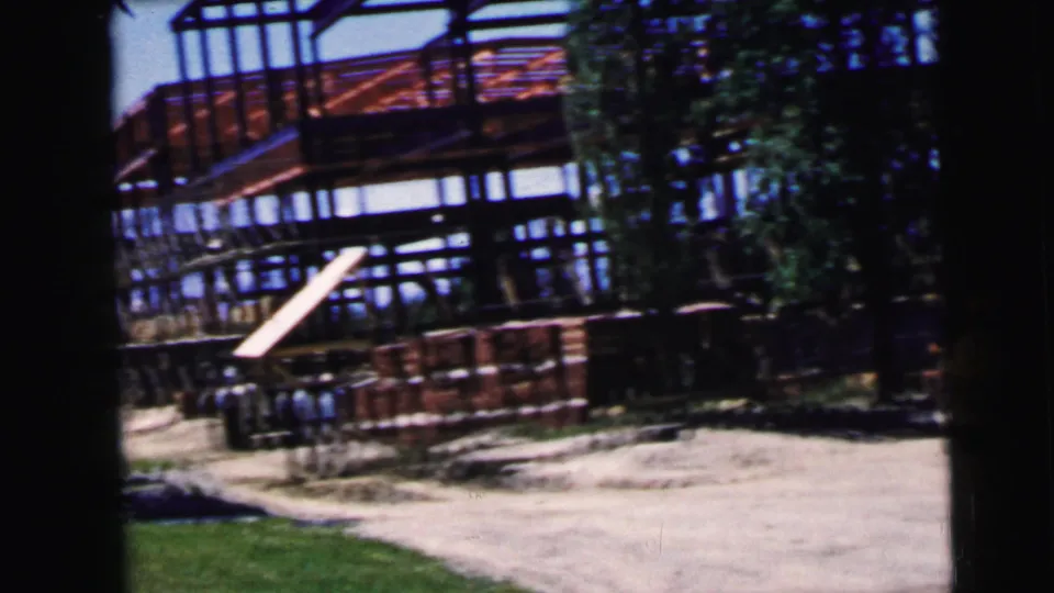 Construction site showing red steel framework and stacked building materials on dirt ground; Camden NJ area, circa 1964