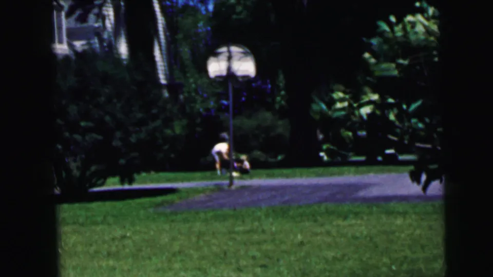 1964 8mm home movie: residential yard with basketball hoop and small figure, paved driveway and shrubs, likely Camden, New Jersey.