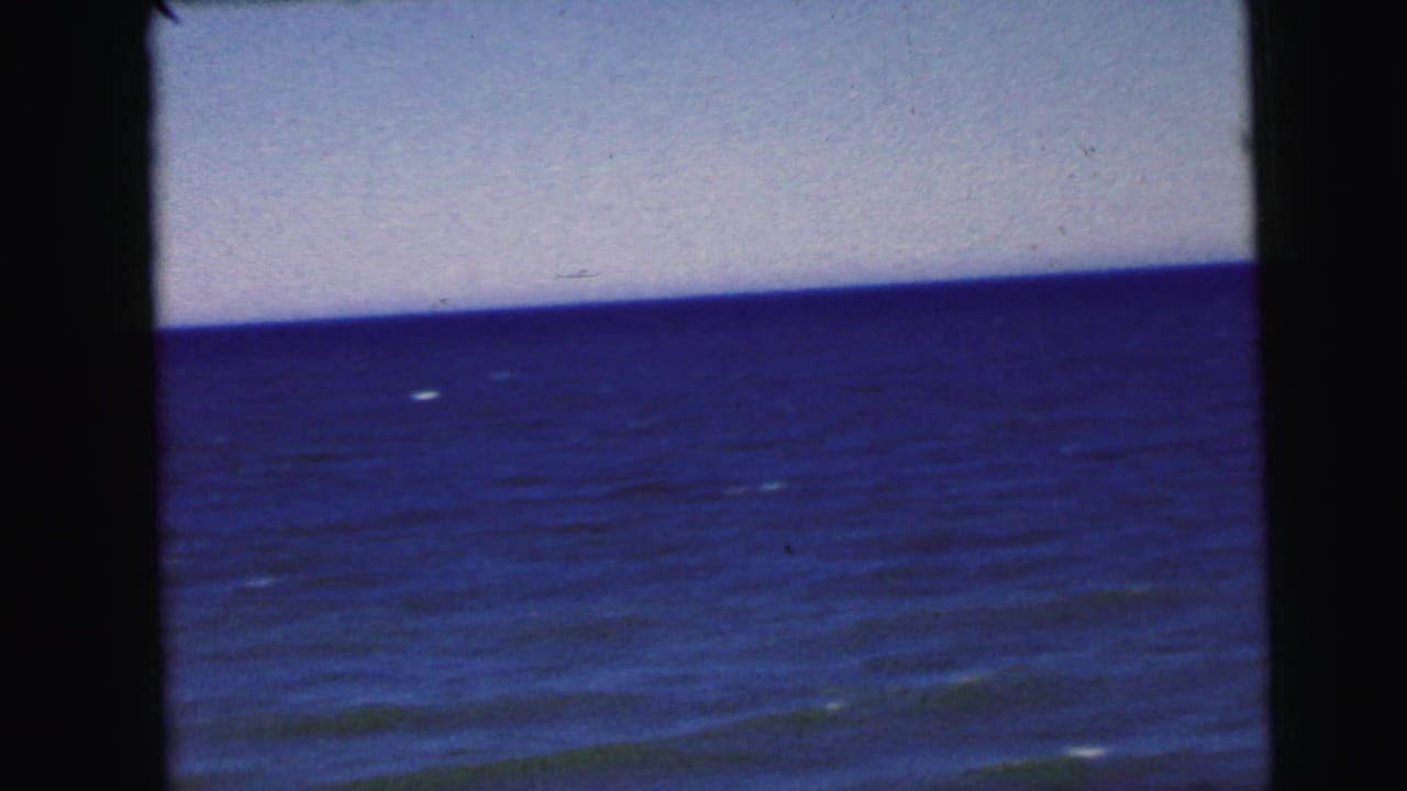Continuing ocean wide shot on 8mm film, circa 1964, from a New Jersey coastal home movie; faint whitecaps dot the calm water.