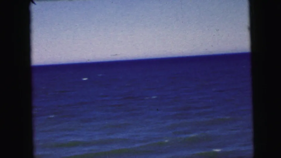 Continuing ocean wide shot on 8mm film, circa 1964, from a New Jersey coastal home movie; faint whitecaps dot the calm water.