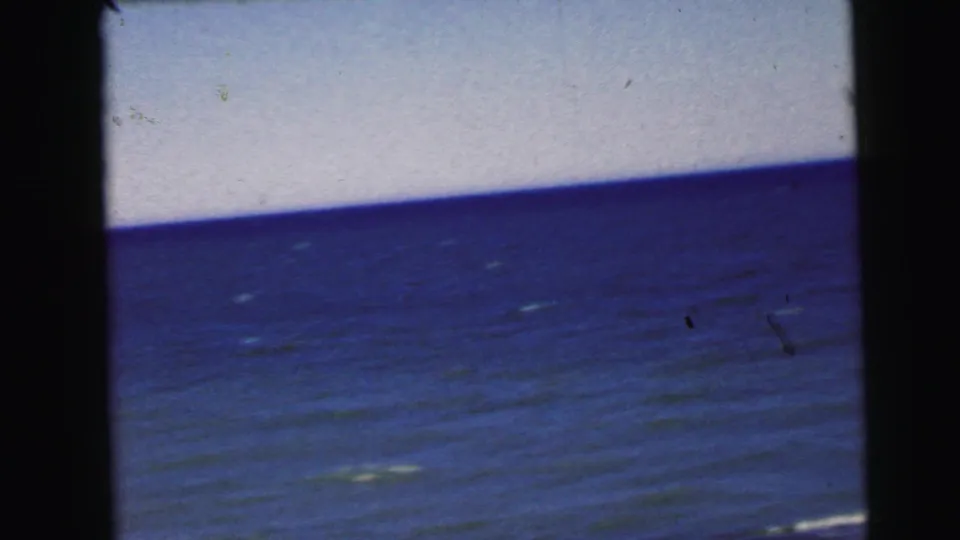8mm home-movie frame circa 1964 showing open water; sky occupies a wider band, emulsion damage visible in upper corner, small ambiguous object at center.