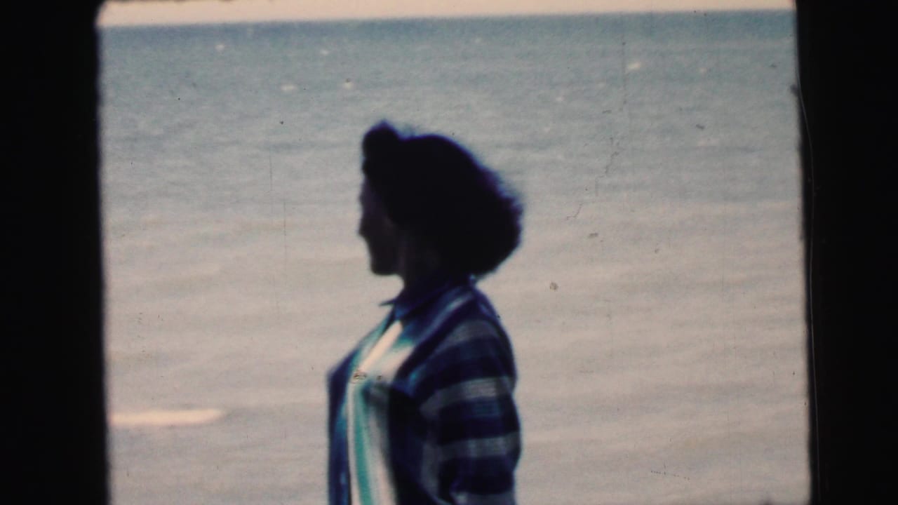 Woman in striped sweater in left profile against calm open water, 8mm color film.