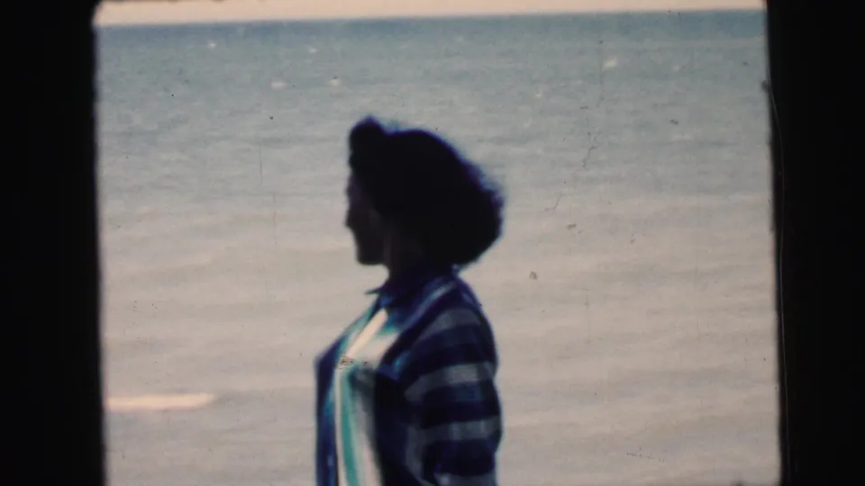 Young woman in left profile wearing a striped knit sweater at the shoreline, 8mm home-movie footage circa 1964, attributed to New Jersey.