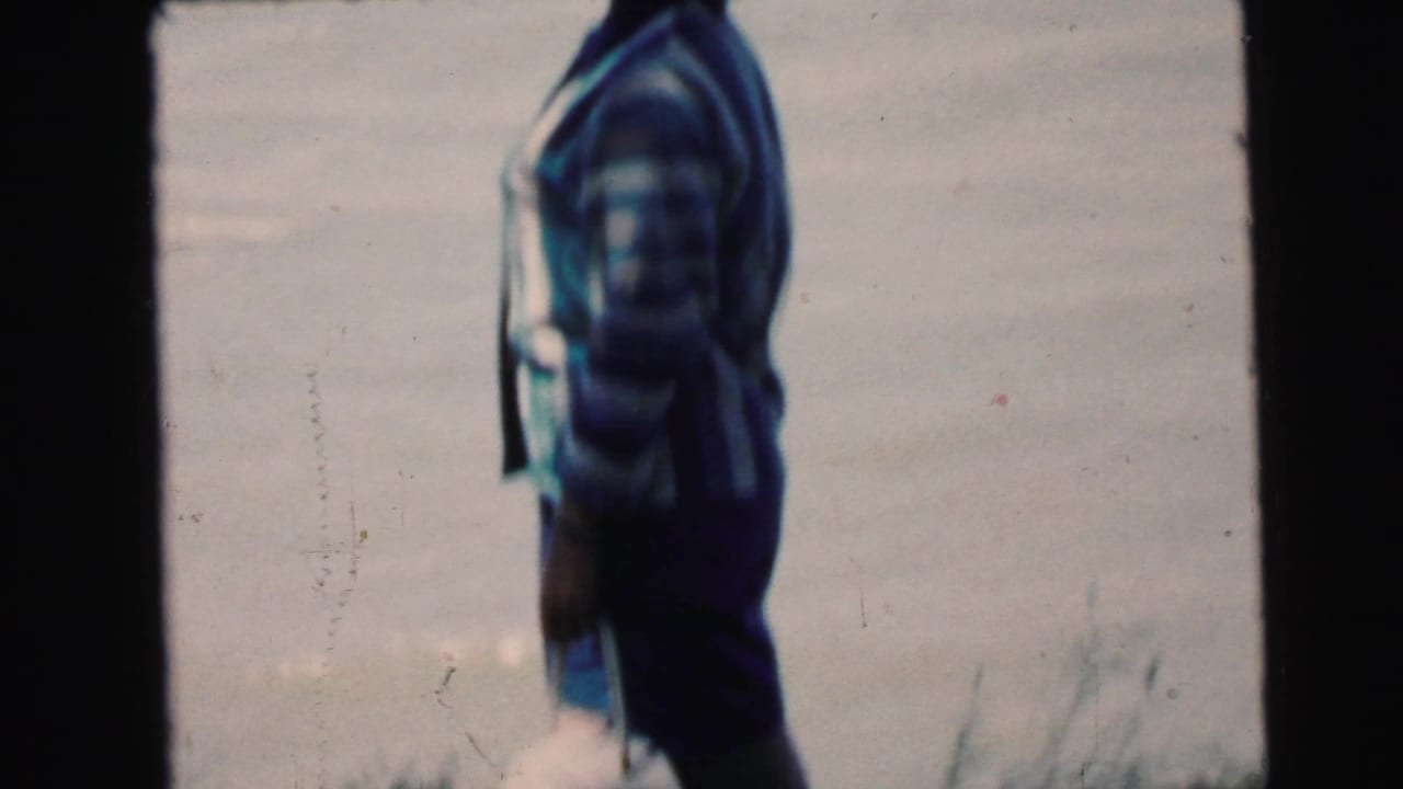 Woman in striped patterned sweater, back to camera, facing open water; film scratches visible on stock.