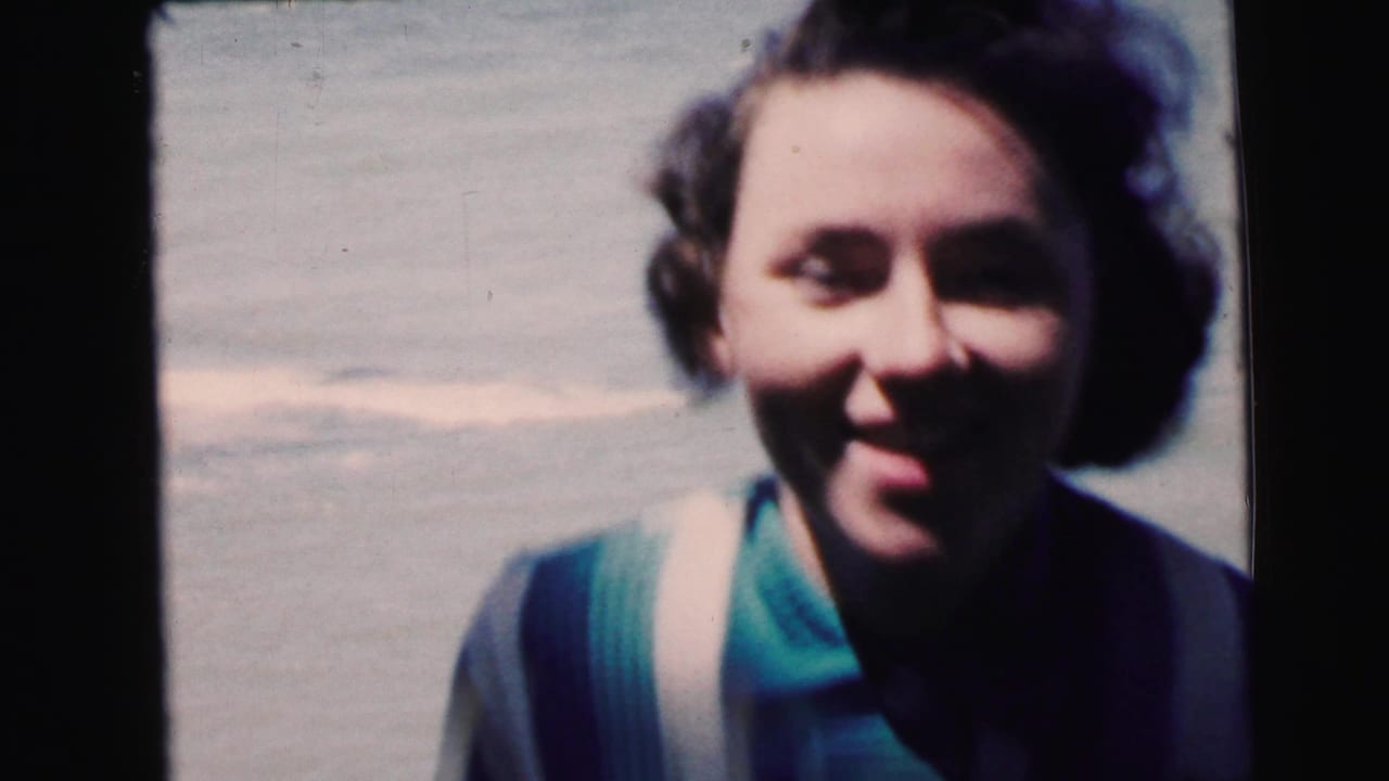 Close-up of a smiling adult woman, slightly out of focus, with short dark hair and a teal scarf, pale sky visible behind her.