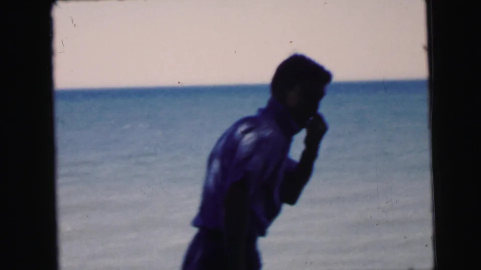 Adult figure in dark top standing by a waterfront, partially turned away, 8mm home movie film, circa 1964, possibly Camden New Jersey.