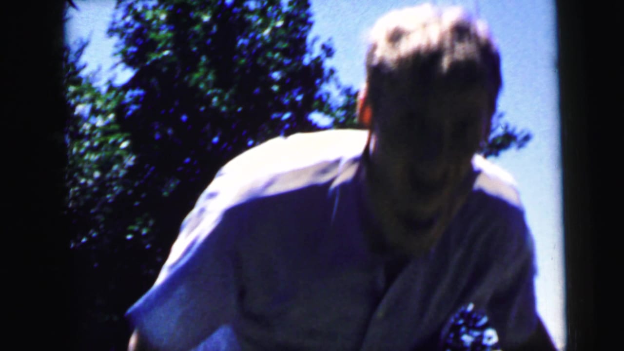A man in a light shirt leans or slides forward near the camera in the Camden 1964 backyard footage.