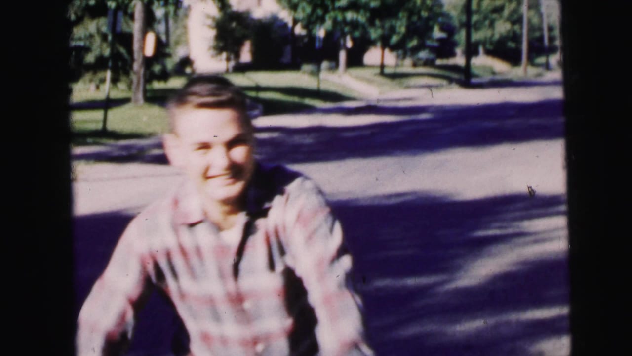 Smiling young man in a plaid shirt running on a tree-lined street.