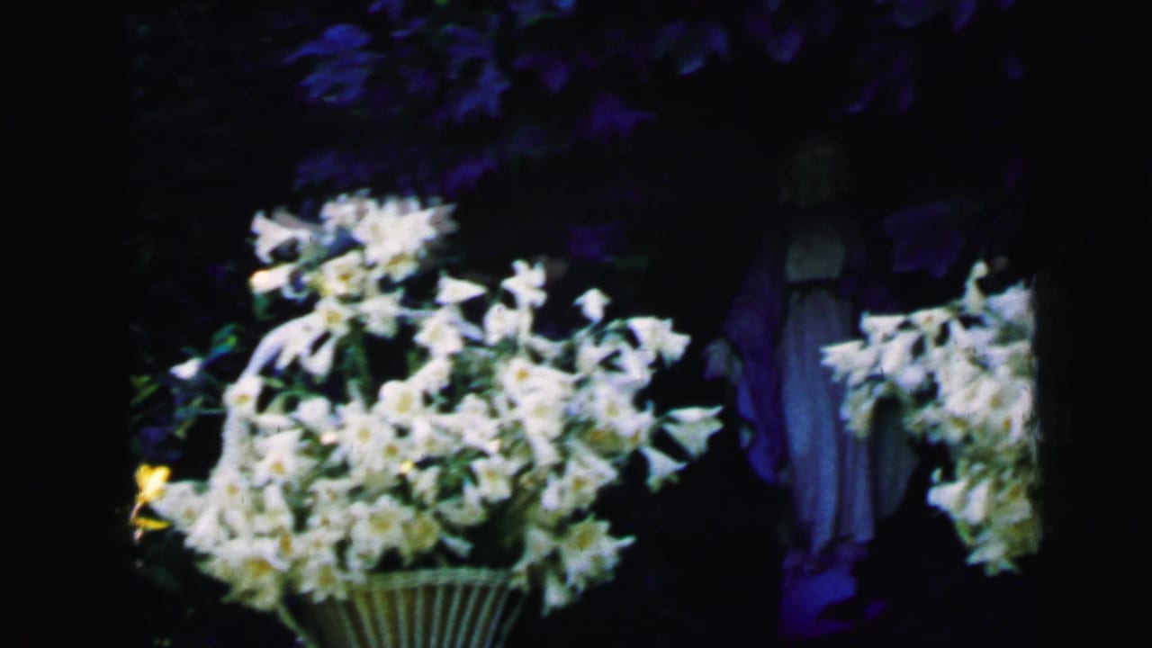 Large white bouquet in a basket with a robed statue partly visible in shadow.