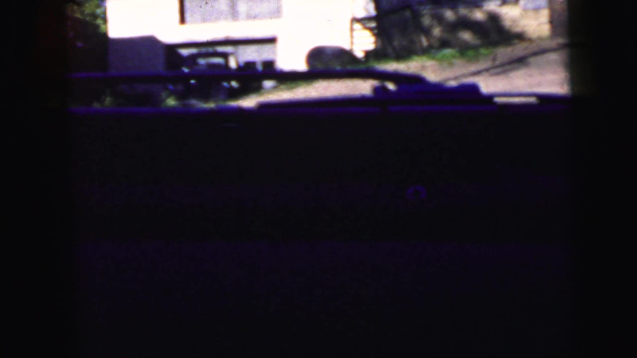 Dark windshield view with a street and pale building partly visible beyond the car interior.