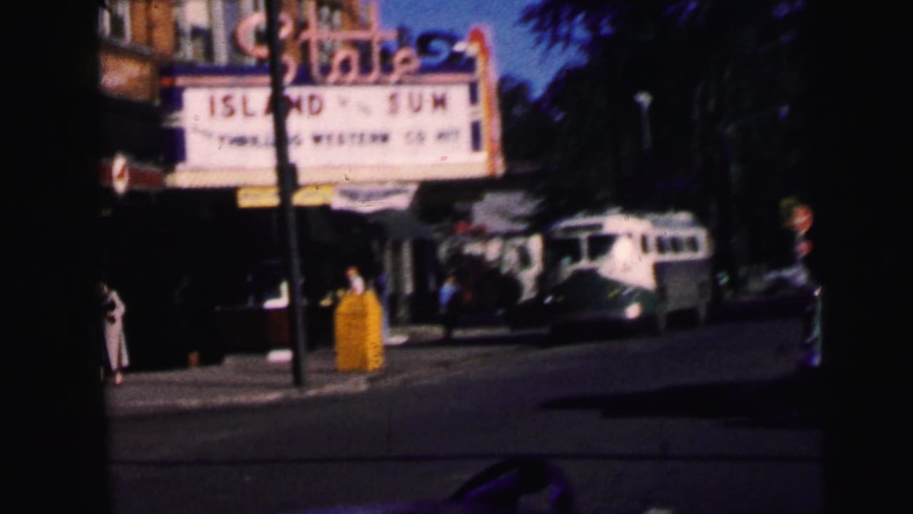 Street view of a theater marquee, sidewalk, bus, and pedestrians from inside a vehicle.
