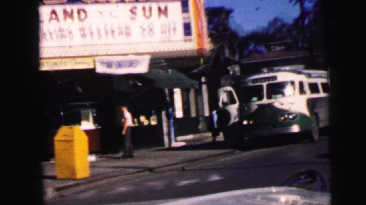 Camden, New Jersey theater frontage with marquee text, bus at curb, pedestrians, and street seen from a car.