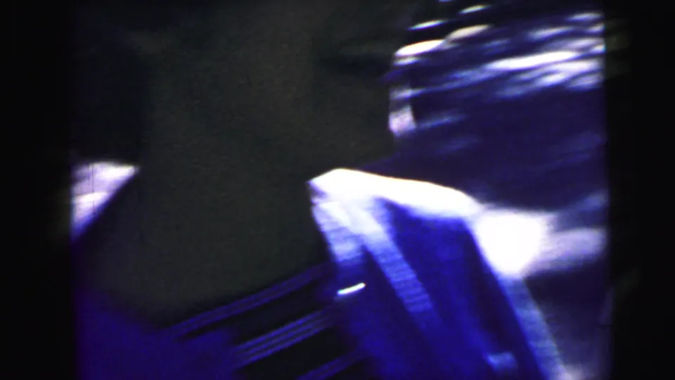 Blurred 8mm frame with a close vehicle surface, bright highlights, and dark window or body shapes near the street.