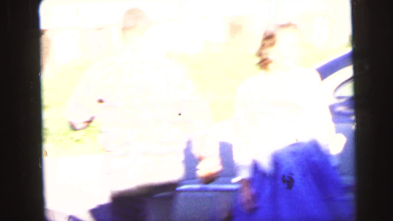 1964 Camden home-movie frame with two women partly washed out by exposure while standing near a parked car.