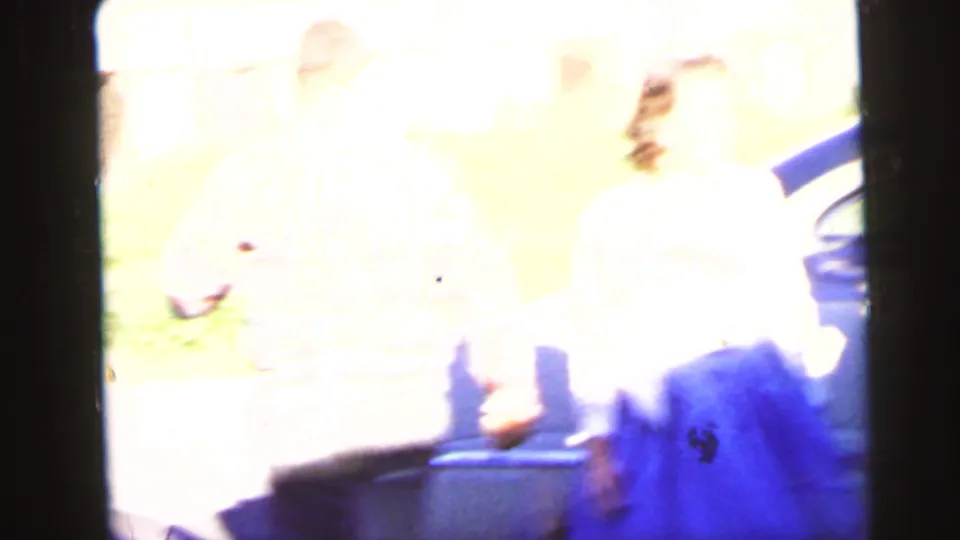1964 Camden home-movie frame with two women partly washed out by exposure while standing near a parked car.