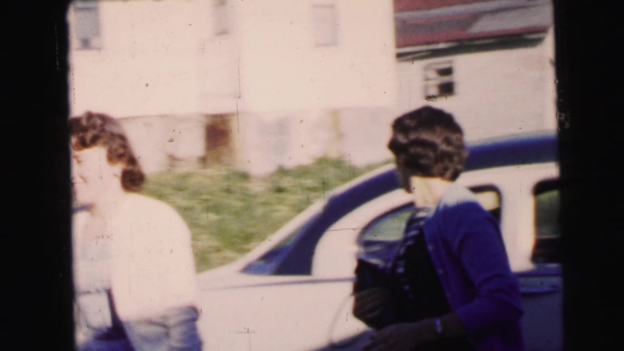 In Camden, New Jersey, two women appear beside a light-colored car on a residential street in 1964 home-movie footage.