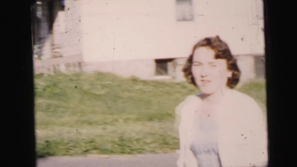 A woman in a light cardigan and blue skirt faces the camera area in a 1964 Camden residential street scene.