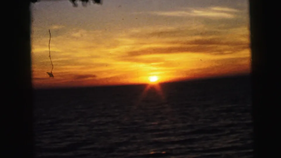 A second sunset frame shows the sun at the waterline, orange clouds, dark sea surface, and visible 8mm film wear.