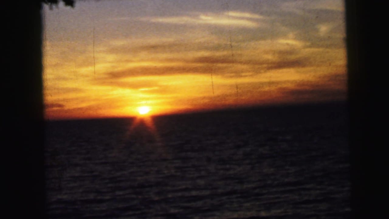 1964 8mm home-movie frame of a low sun over ocean water, seen through dark vertical frame edges in the Camden, New Jersey clip metadata.