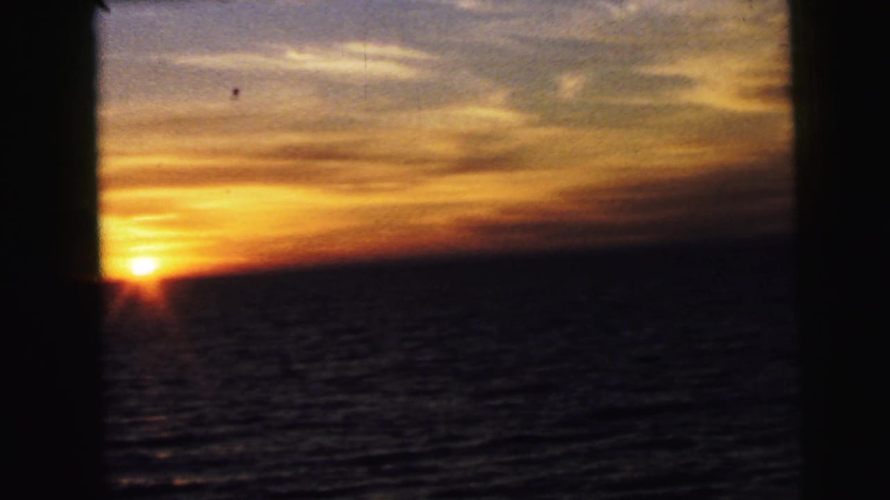 A fixed 8mm view shows the sun touching the ocean horizon with warm clouds above and heavy dark borders in frame.