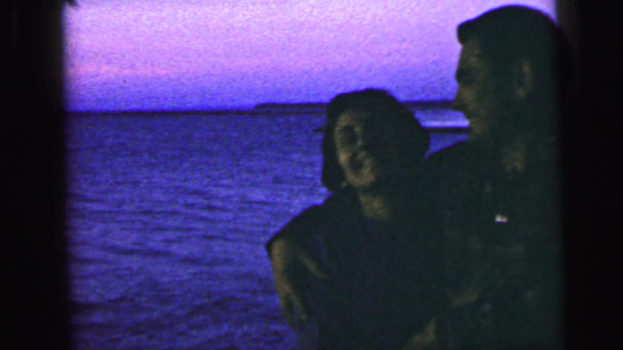 The couple remains close in the 1964 Camden waterfront scene, partly silhouetted against open water and evening sky.