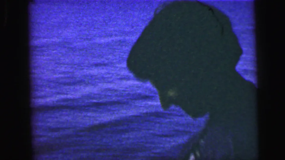 One adult is shown in close side profile near the water, with heavy shadow and color cast from the 8mm footage.