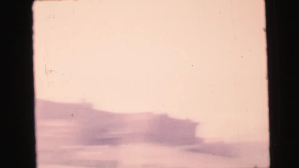 1964 Camden home-movie frame looking through dark window bars toward a soft, overexposed urban building exterior.