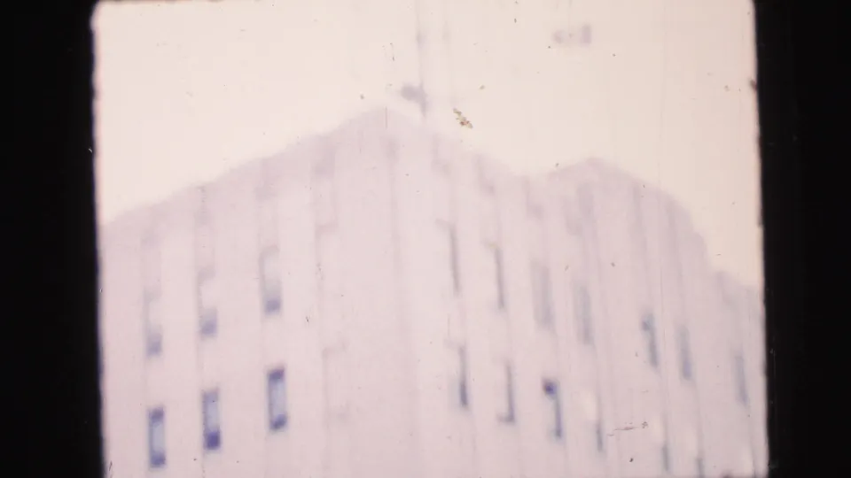 Soft 8mm frame of a pale apartment building in Camden, with dark windows and a strong window bar in the foreground.