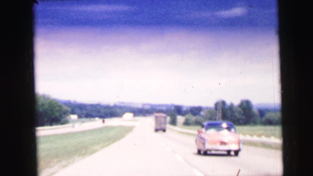 Pink classic car and truck traveling on a divided rural highway.